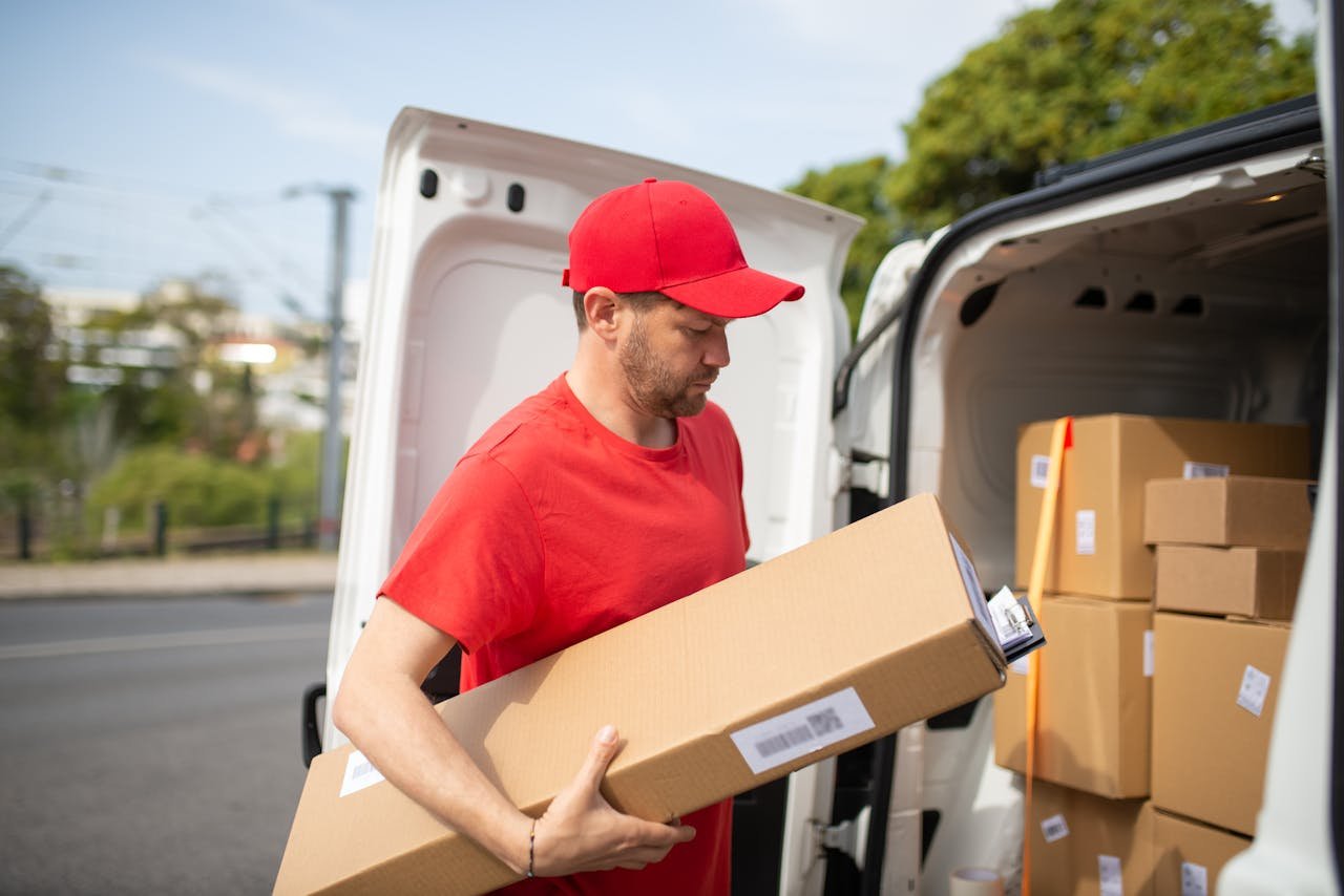 A Man in Red Shirt Carrying a Cardboard Box Beside the Van